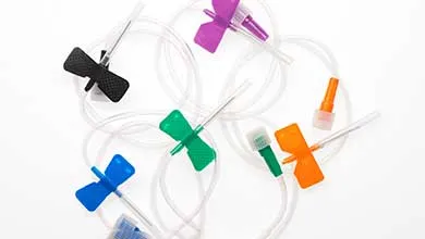 Several butterfly needles with purple, black, green, blue, and orange wings are scattered on a white surface, with their clear tubing tangled together.